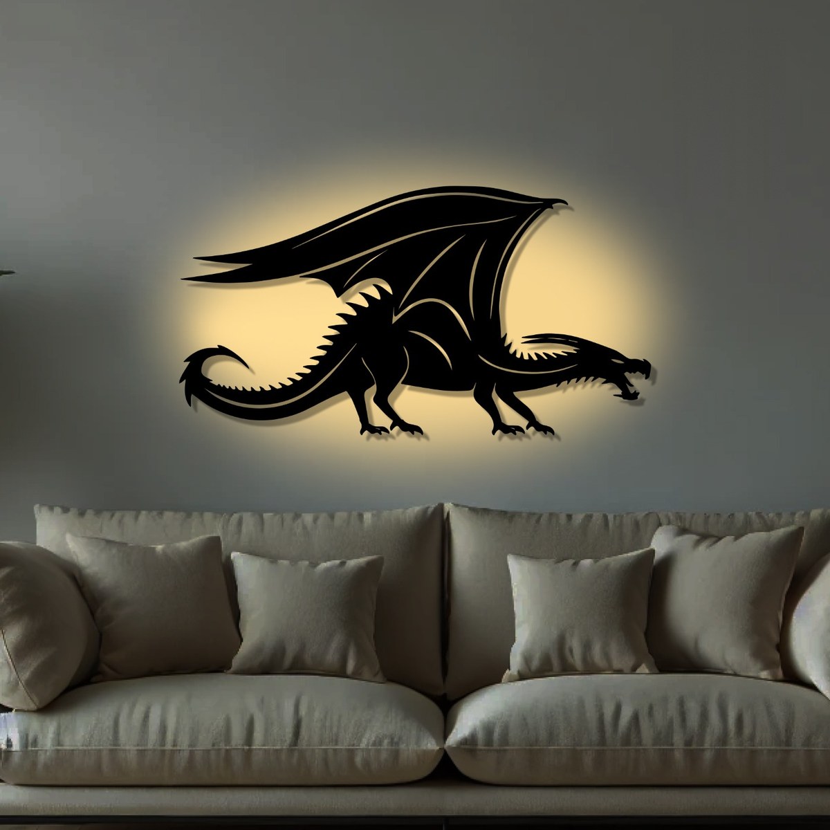 Dragon wall art: black laser-cut metal shadow dragon with a raised wing, shown with a warm glow behind it above a grey sofa